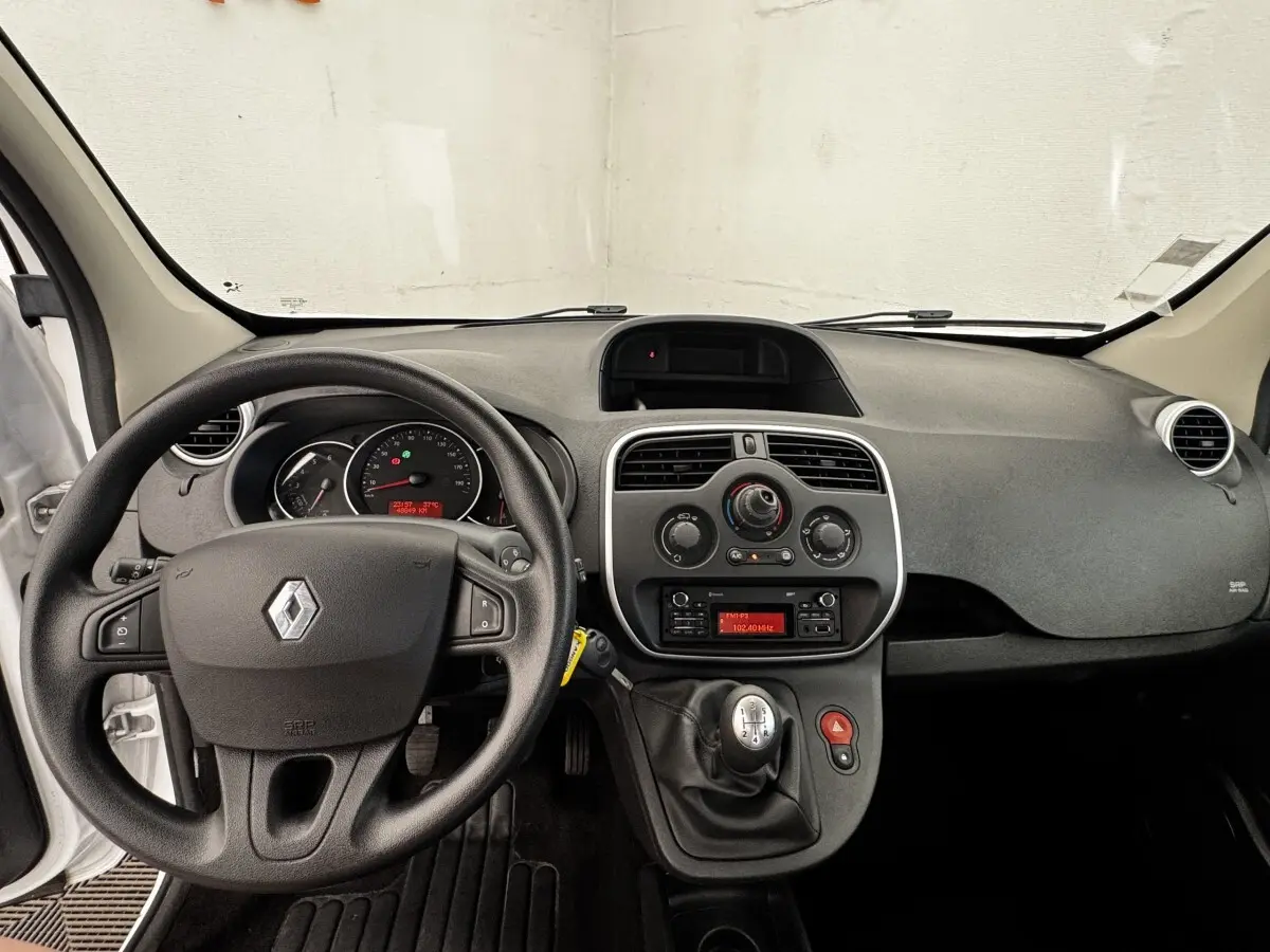 Vue intérieure avant du tableau de bord et volant noir d’un Renault Kangoo blanc de 2016 avec boîte manuelle.