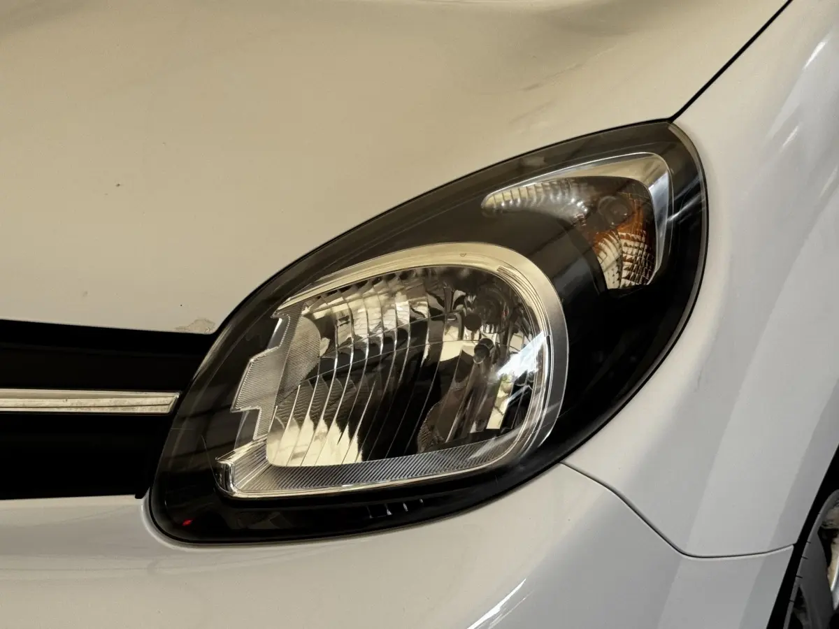 Gros plan sur le phare avant droit du Renault Kangoo blanc, mettant en valeur les détails du bloc optique.