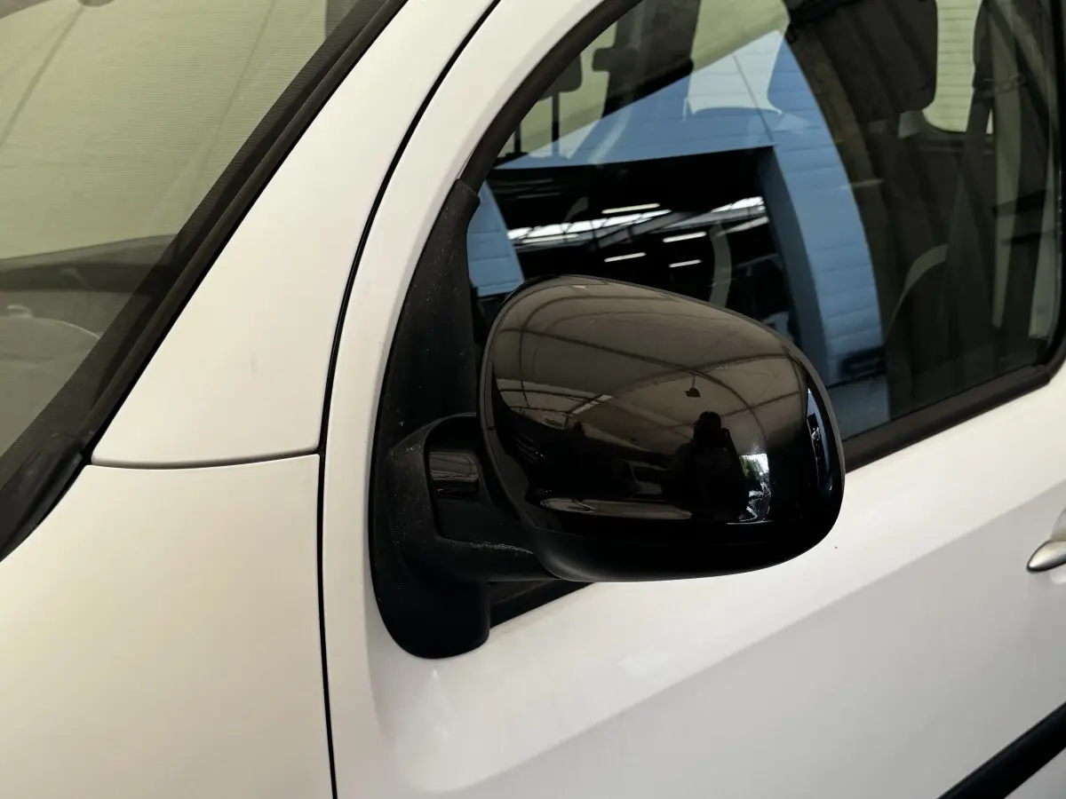 Gros plan sur le rétroviseur noir côté conducteur d’un Renault Kangoo blanc, vue latérale avant.