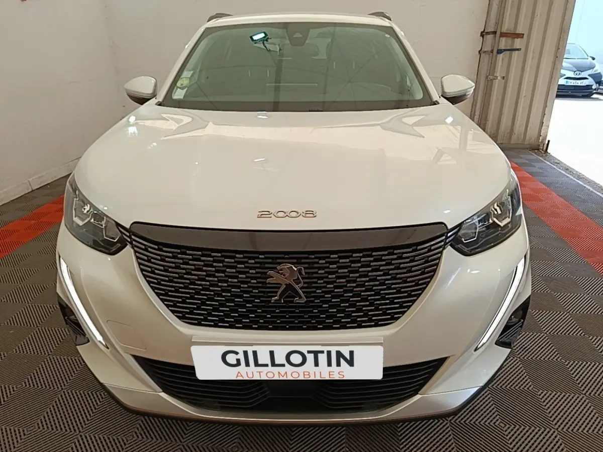 Vue avant d'une Peugeot 2008 blanche avec calandre noire et feux LED en intérieur de garage.