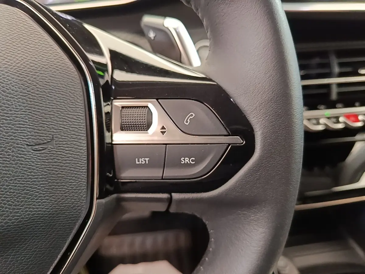 Gros plan sur le volant cuir noir multifonctions du Peugeot 2008, avec commandes audio et téléphone intégrées.