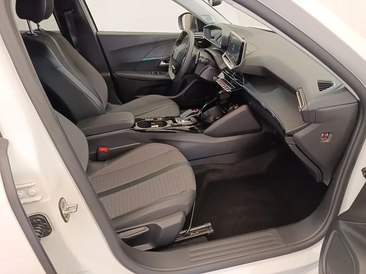 Vue intérieure côté conducteur du Peugeot 2008 blanc 2021, sièges tissu gris et tableau de bord avec écran tactile.