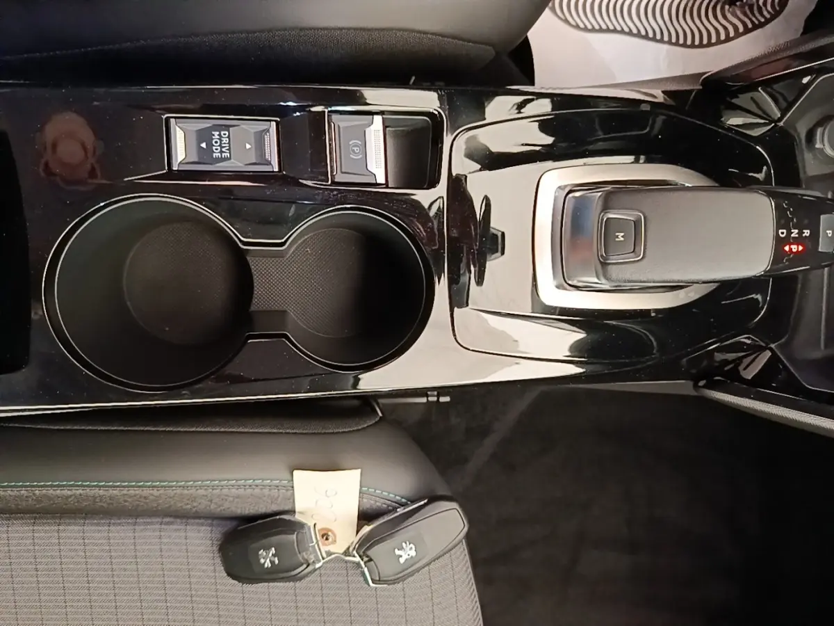 Vue rapprochée de la console centrale noire brillante avec levier de vitesse automatique et porte-gobelets du Peugeot 2008 blanc.