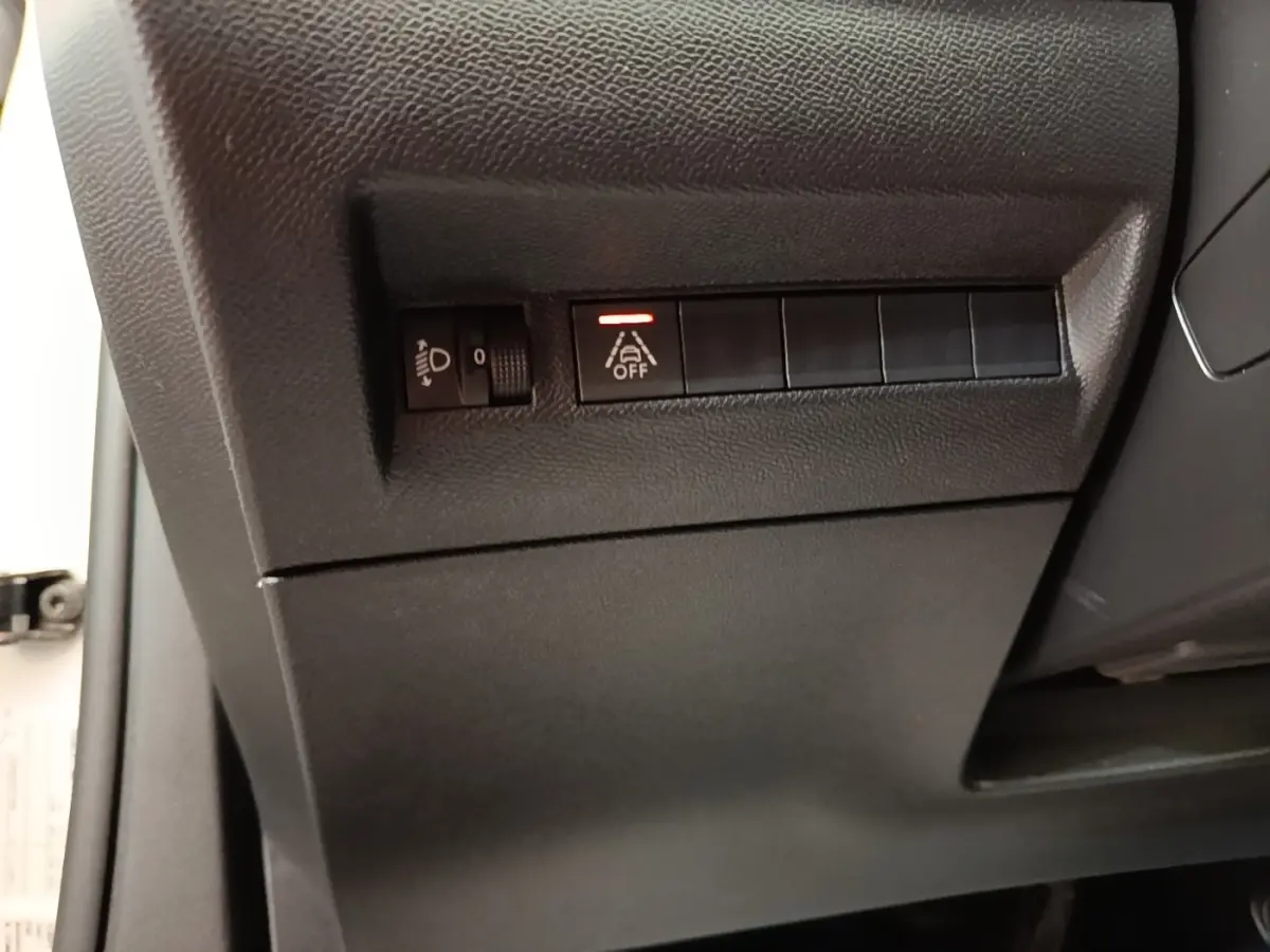 Détail des commandes côté gauche sous le tableau de bord d’un Peugeot 2008 blanc, bouton d’aide à la conduite activé.