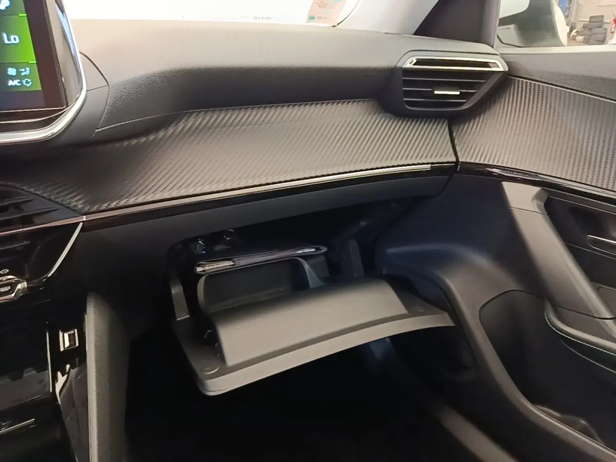 Vue intérieure côté passager du tableau de bord noir et boîte à gants ouverte avec rangement dans une Peugeot 2008 blanche.