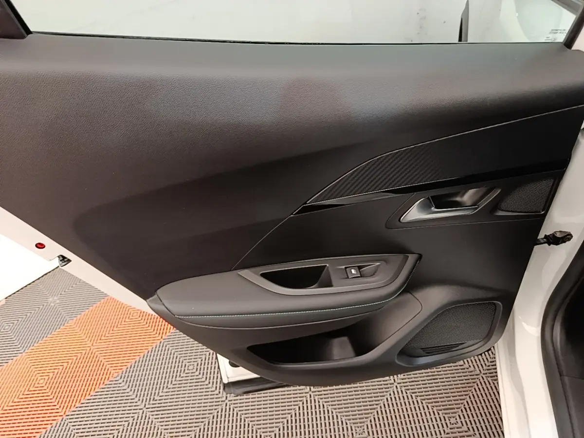 Vue intérieure côté gauche de la porte avant d'une Peugeot 2008 blanche avec garniture noire et commande de fenêtre.