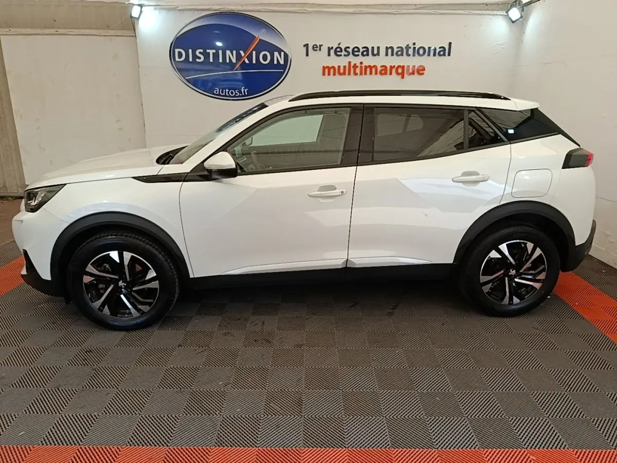 Vue latérale droite d'un Peugeot 2008 blanc 2021 avec jantes noires et toit noir contrasté en intérieur showroom.