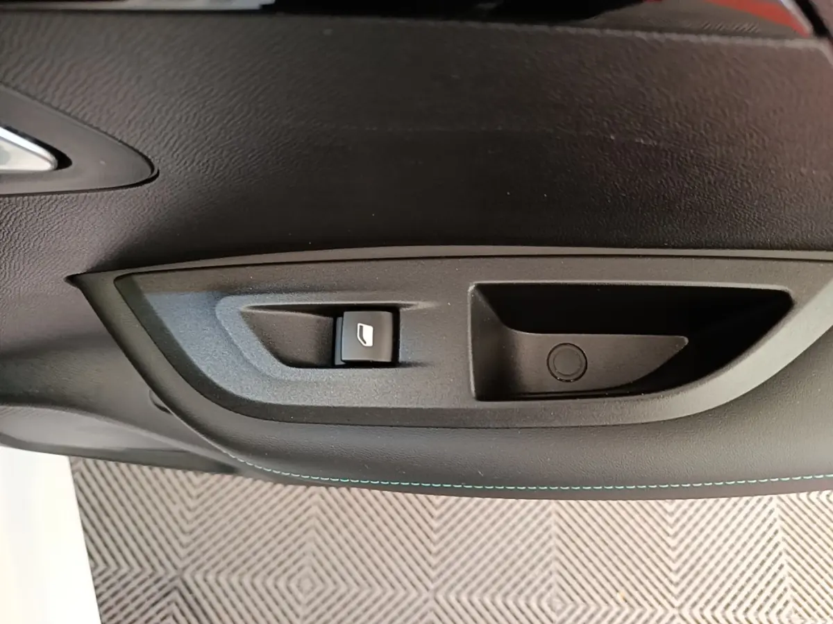 Gros plan sur la commande de lève-vitre côté conducteur du Peugeot 2008 blanc, avec surpiqûres bleues visibles.