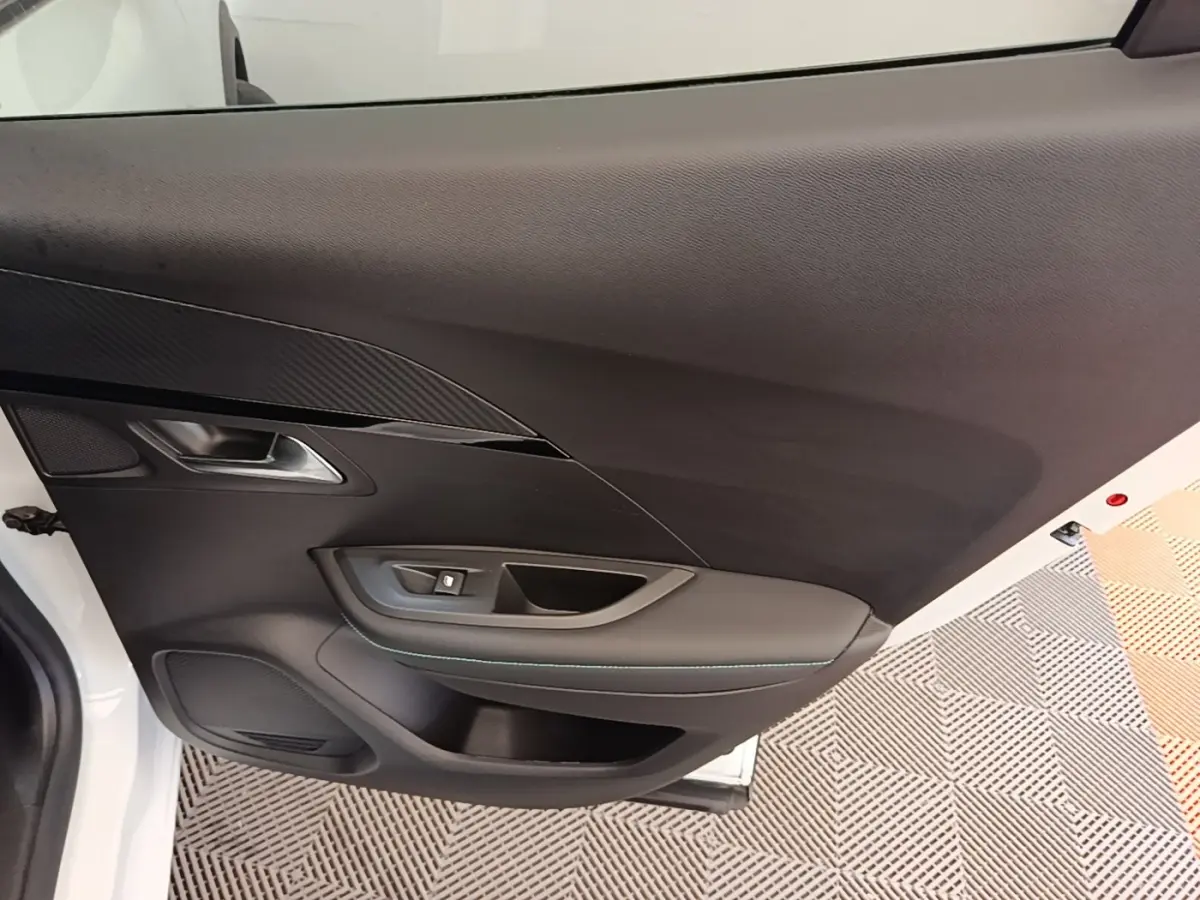 Vue intérieure sur la porte avant gauche noire d’un Peugeot 2008 blanc, avec poignée et commande de vitre.
