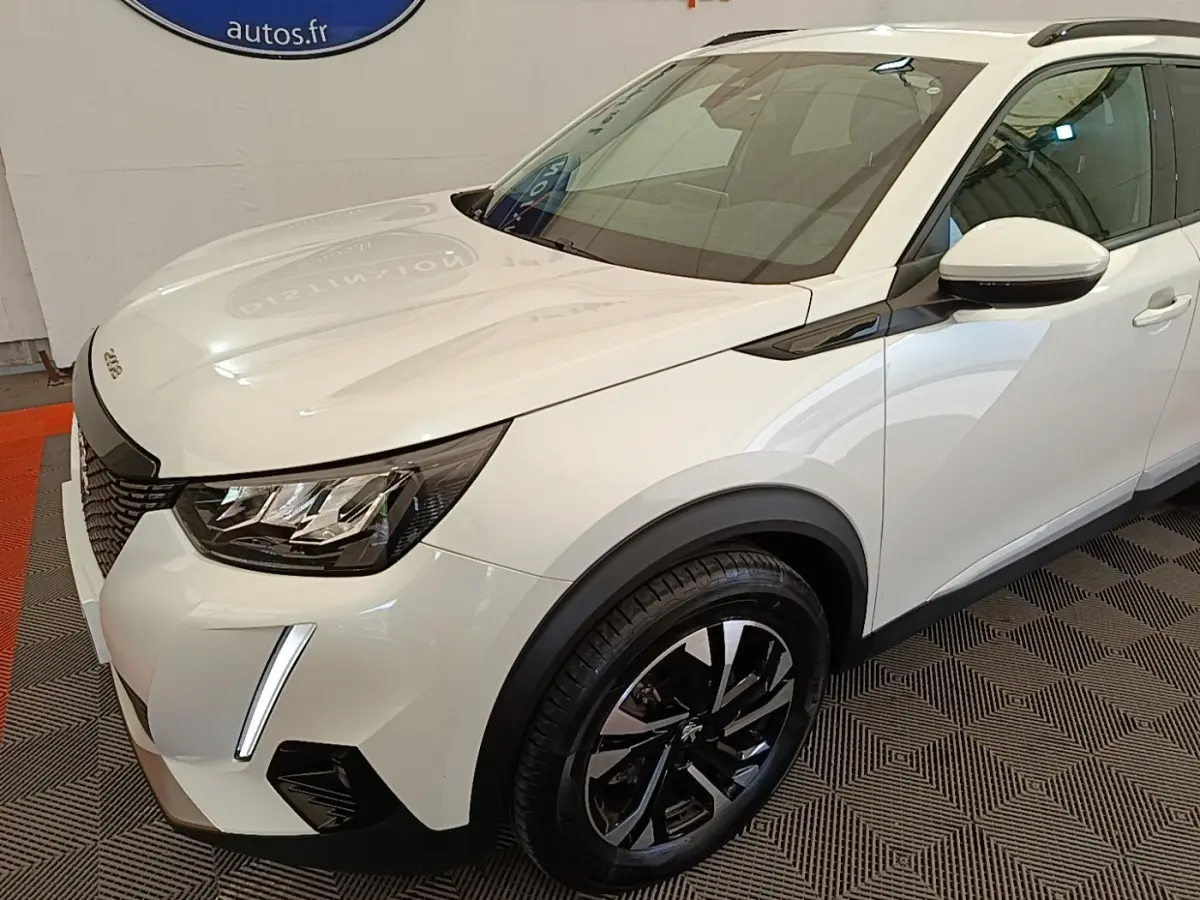 Vue 3/4 avant droit d’un Peugeot 2008 blanc avec phares LED et jantes alliage noires brillantes.