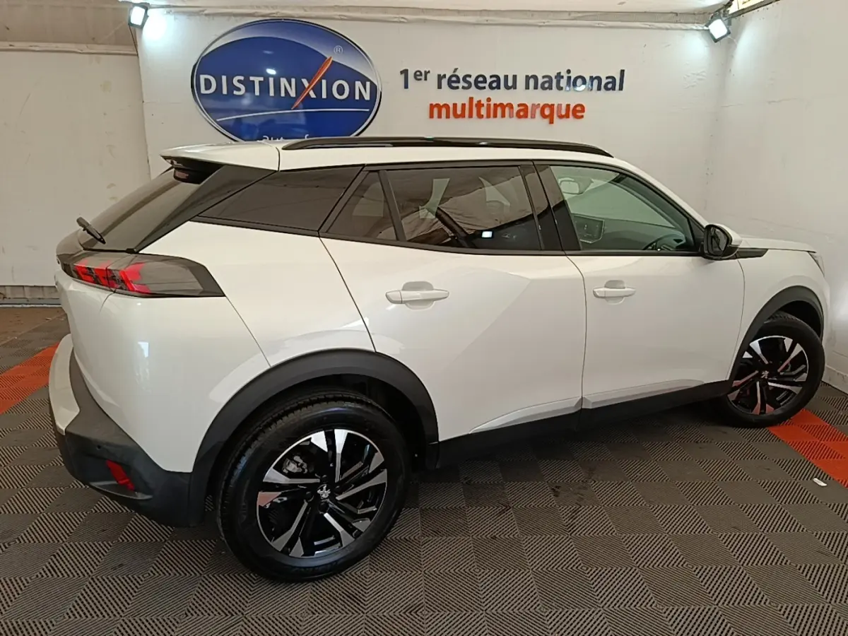 Peugeot 2008 blanc vue de profil droit en intérieur, avec toit noir et jantes alliage bicolores.