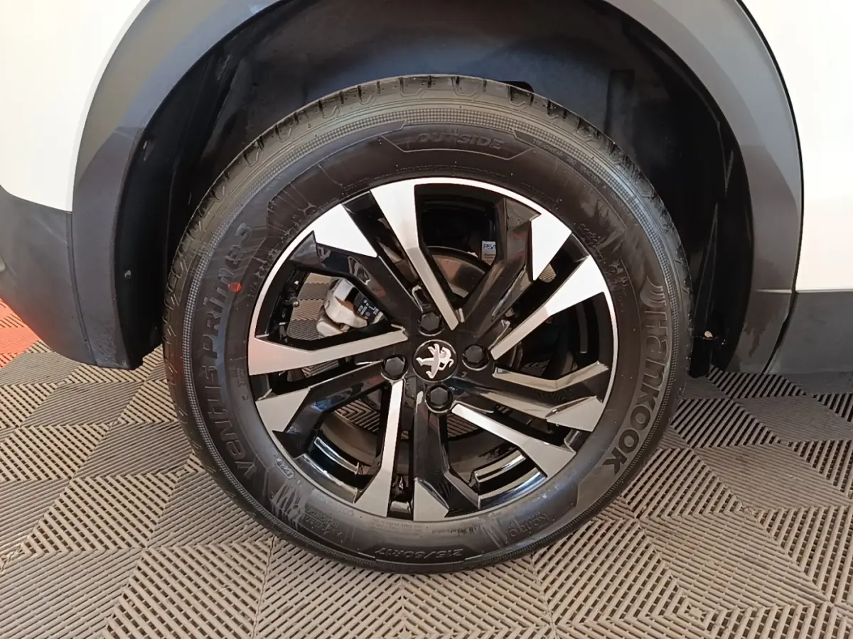 Gros plan sur la roue avant droite du Peugeot 2008 blanc, avec jante alliage noire et argentée au design moderne.