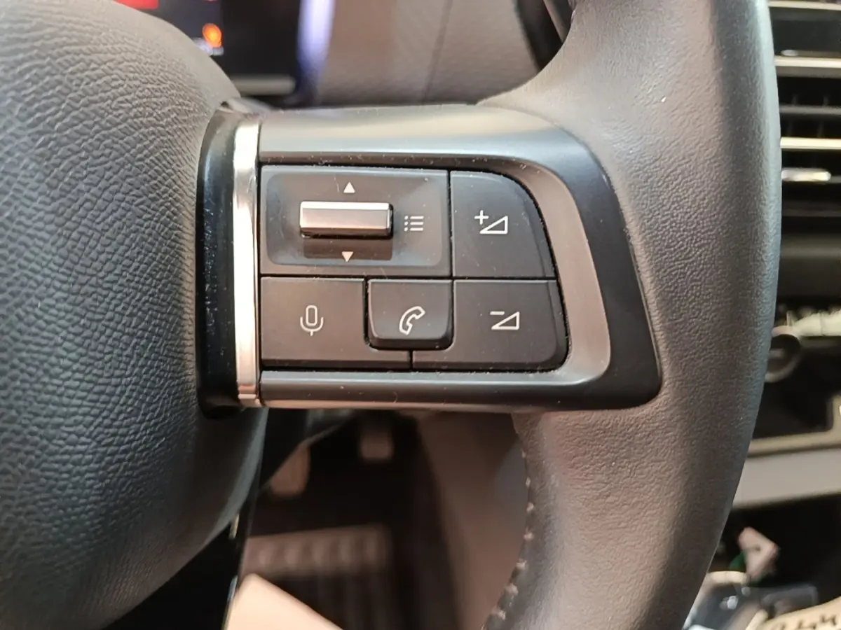 Gros plan sur les commandes multifonctions en cuir du volant côté gauche d'une Citroën C4 gris clair.