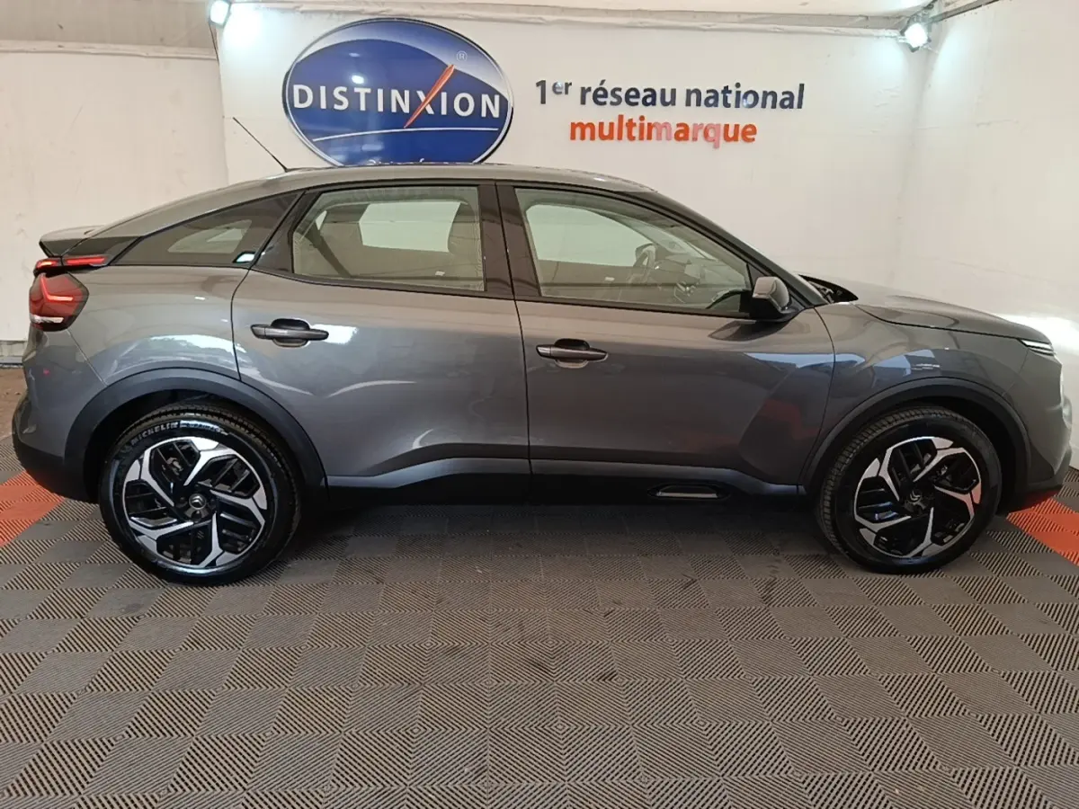Profil droit d'une Citroën C4 gris clair 2021 avec jantes noires et toit plongeant dans un showroom.