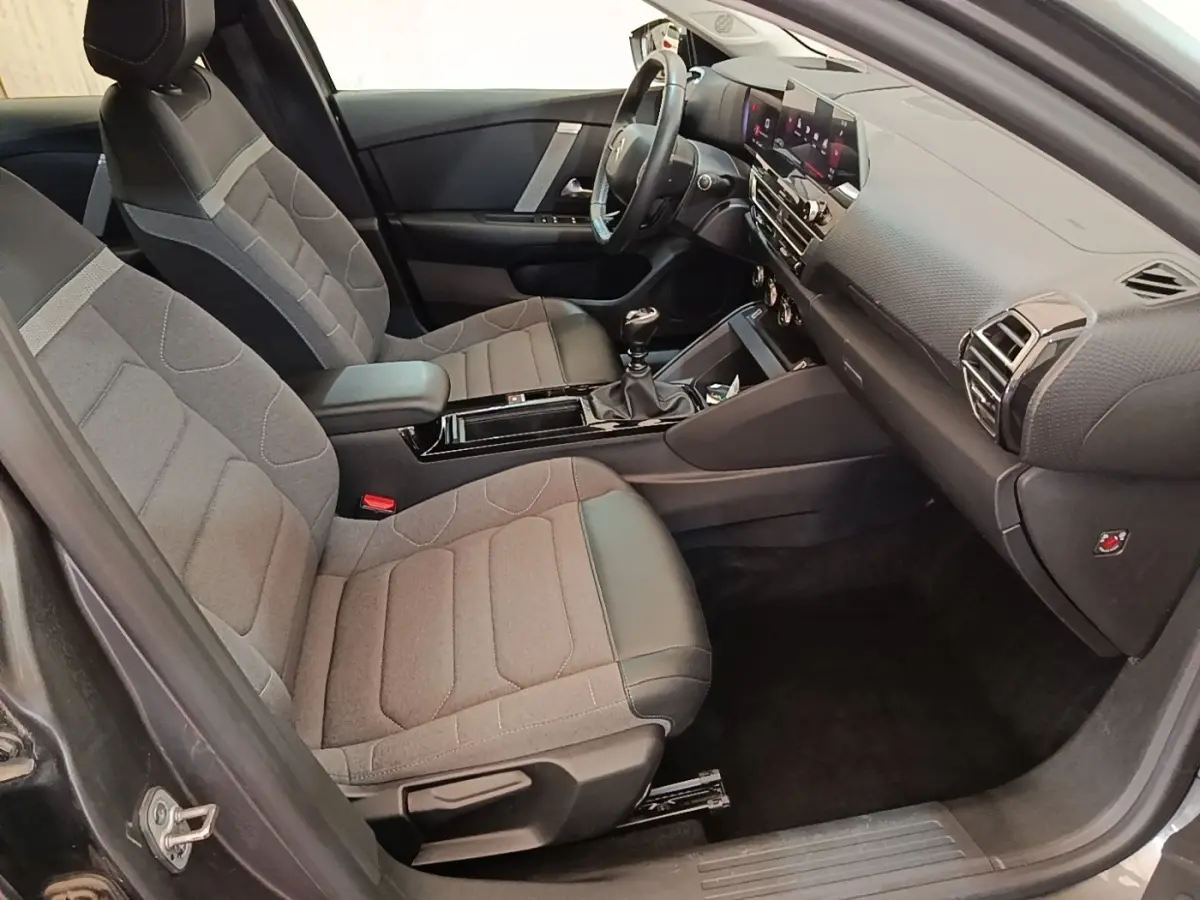 Vue intérieure côté conducteur de la Citroën C4 gris clair, avec sièges tissu et cuir, volant multifonctions et tableau de bord numérique.