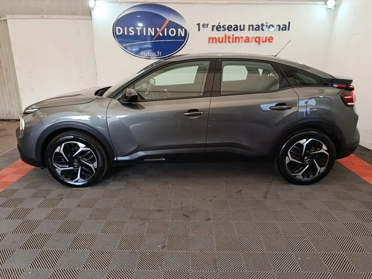Profil côté gauche d'une Citroën C4 gris clair 2021 avec jantes noires et toit noir, en intérieur showroom.