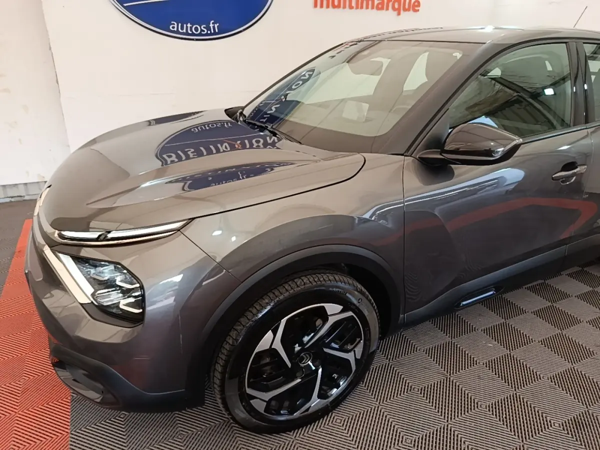 Vue 3/4 avant droit d'une Citroën C4 gris clair avec jantes noires et détails modernes au showroom.