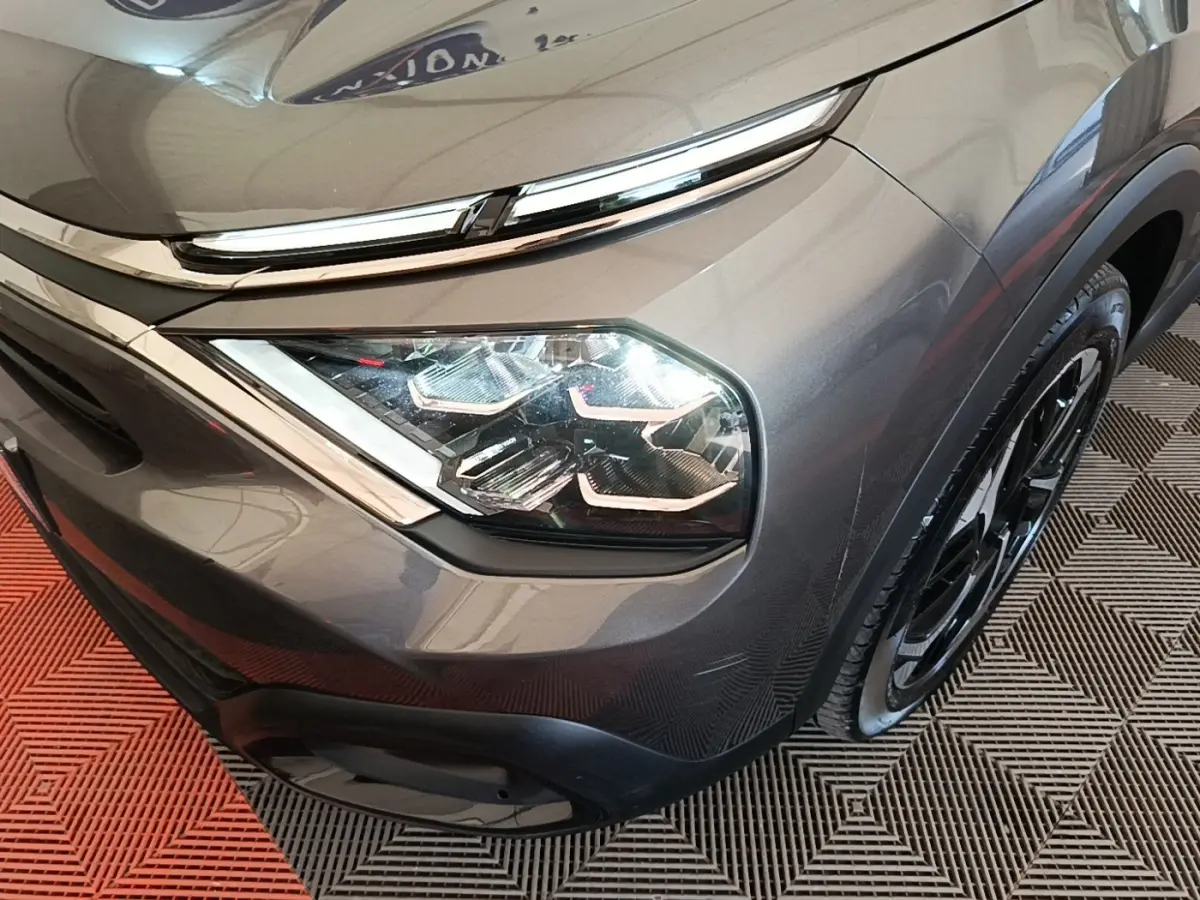 Gros plan sur le phare avant droit et la calandre d'une Citroën C4 gris clair, avec jante noire visible.