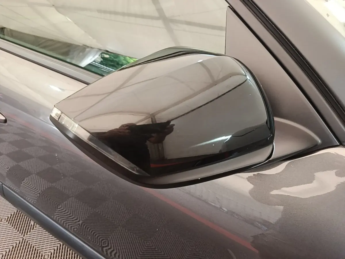 Rétroviseur droit noir brillant sur Citroën C4 gris clair, vue rapprochée avec reflet de l'environnement.