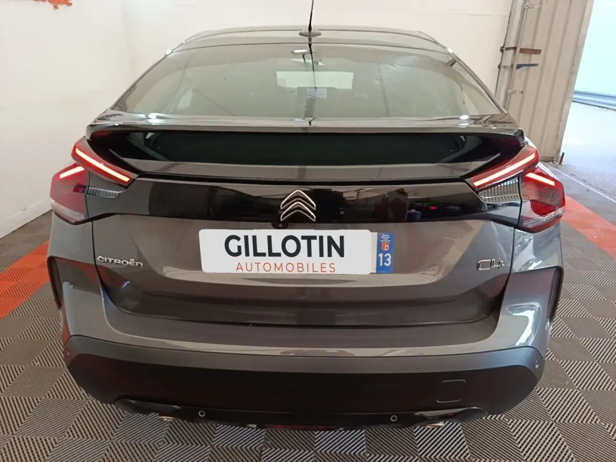 Vue arrière d'une Citroën C4 gris clair 2021 avec feux LED et spoiler de coffre en intérieur showroom.