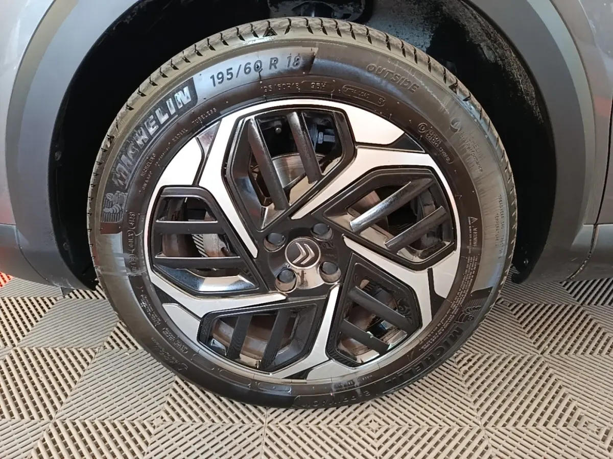 Gros plan sur la roue avant droite d’une Citroën C4 gris clair avec jante alliage au design géométrique noir et argent.