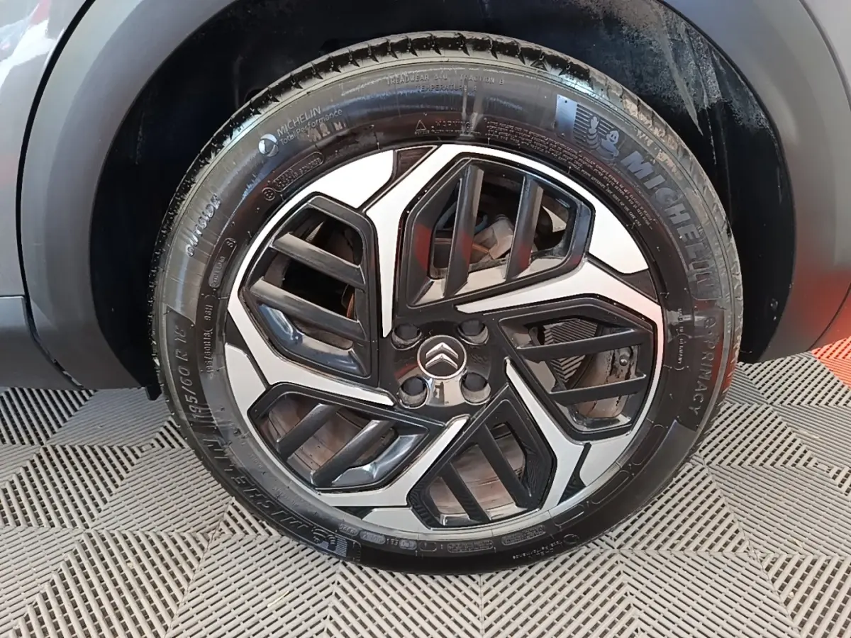 Gros plan sur la roue avant droite d’une Citroën C4 gris clair avec jante alliage au design géométrique noir et argent.