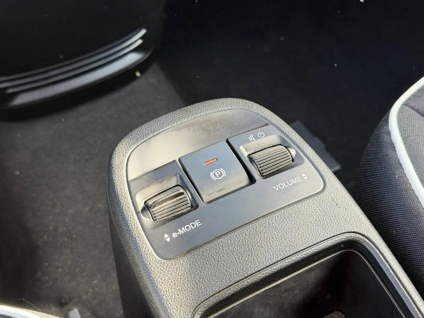 Gros plan sur la console centrale avec commandes e-MODE et volume, siège tissu noir monogramme Fiat visible à droite.