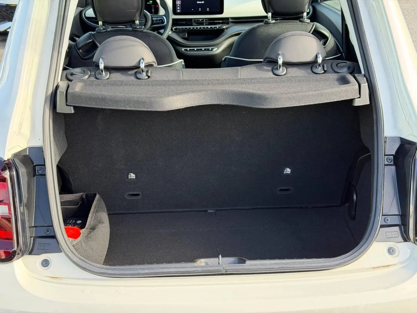 Coffre ouvert vu de l'arrière d'une FIAT 500 e 118ch Ice White pastel, montrant l'intérieur noir et tablette cache-bagages.