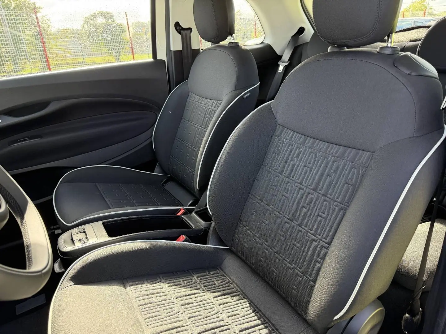 Vue intérieure des sièges avant noirs avec motif monogramme Fiat et surpiqûres blanches dans une Fiat 500 e 118ch MY24.