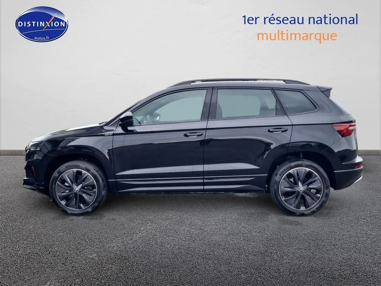 Profil côté gauche d'un SUV SKODA KAROQ noir 2025 avec jantes alu et barres de toit visibles sur fond neutre.