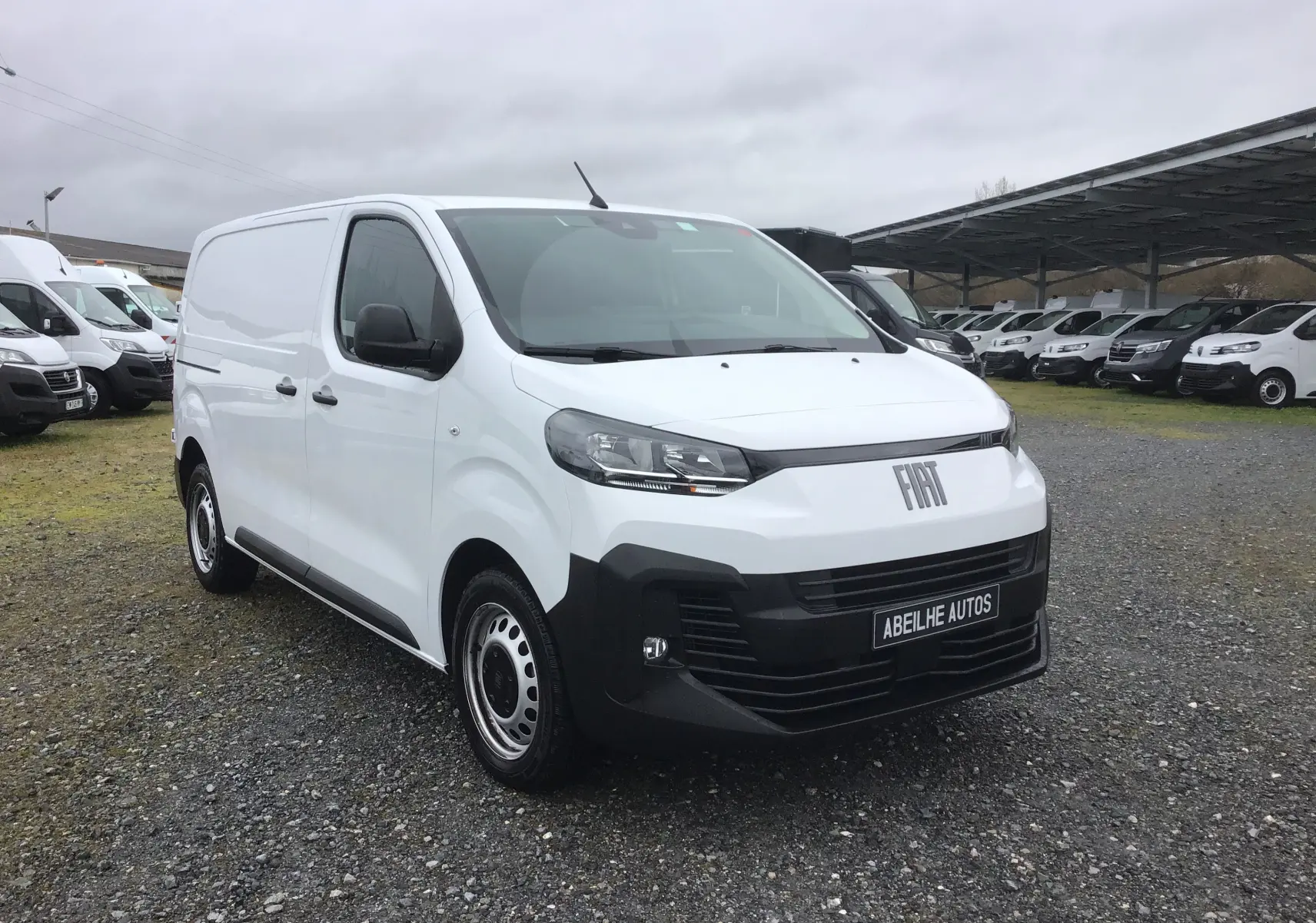 Vue 3/4 avant d’un FIAT Scudo Fourgon blanc 2024 avec pare-chocs noir et jantes acier, sur parking extérieur.