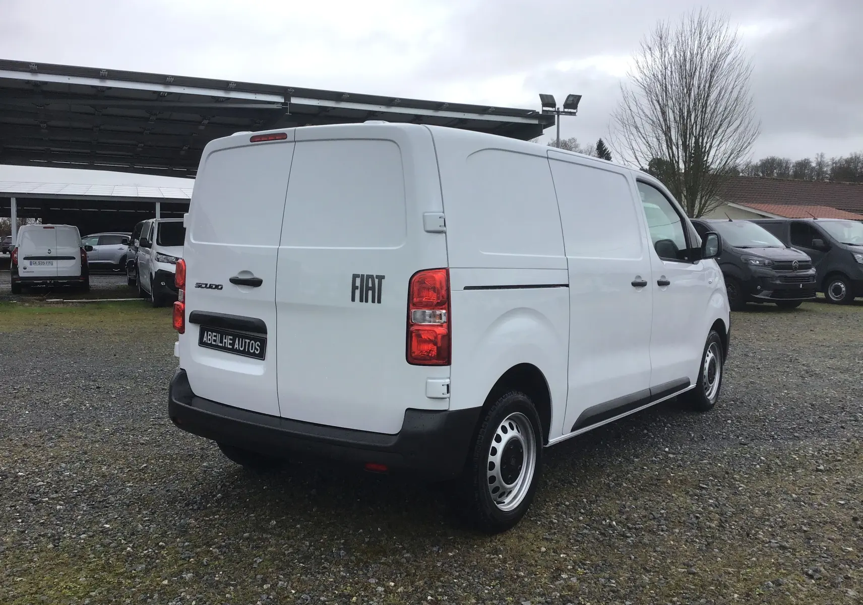 Vue 3/4 arrière droite d'un FIAT Scudo Fourgon blanc 2024 avec hayon fermé et protections noires sur un parking.