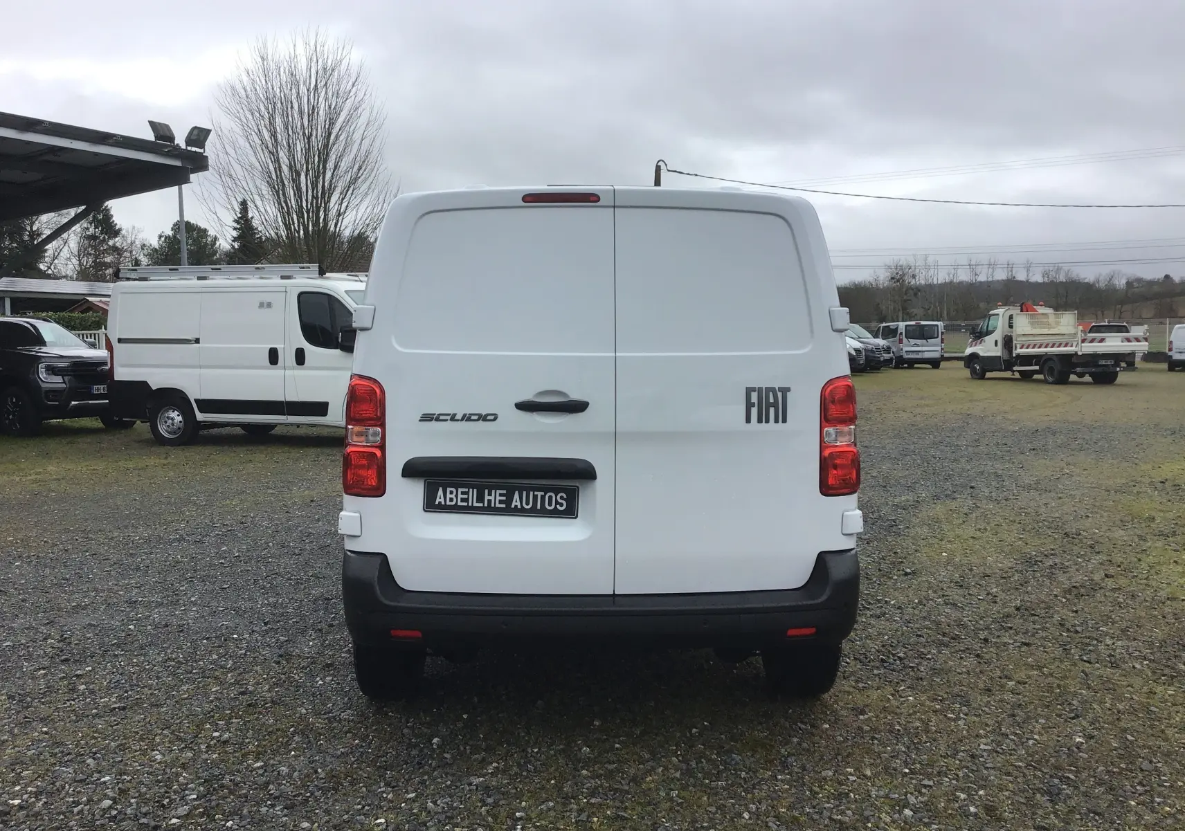 Vue arrière d’un FIAT Scudo fourgon blanc 2024 avec porte battante et pare-chocs noir sur un terrain extérieur.