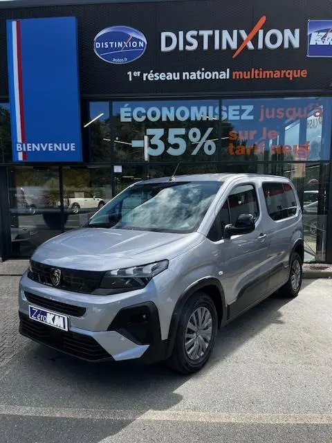 Peugeot Rifter gris foncé en 3/4 avant droit, garé devant une concession avec enseigne Distinxion visible.