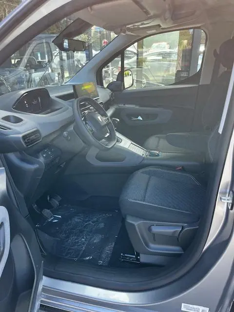 Intérieur avant droit du Peugeot Rifter gris foncé 2024, volant multifonctions, tableau de bord digital et siège tissu noir.