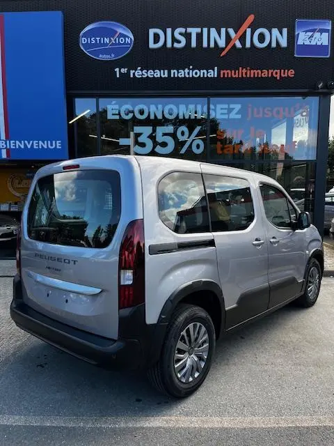 Vue 3/4 arrière droite d’un Peugeot Rifter gris foncé 2024 avec vitres opaques et rails de toit, stationné devant une concession multimarque.