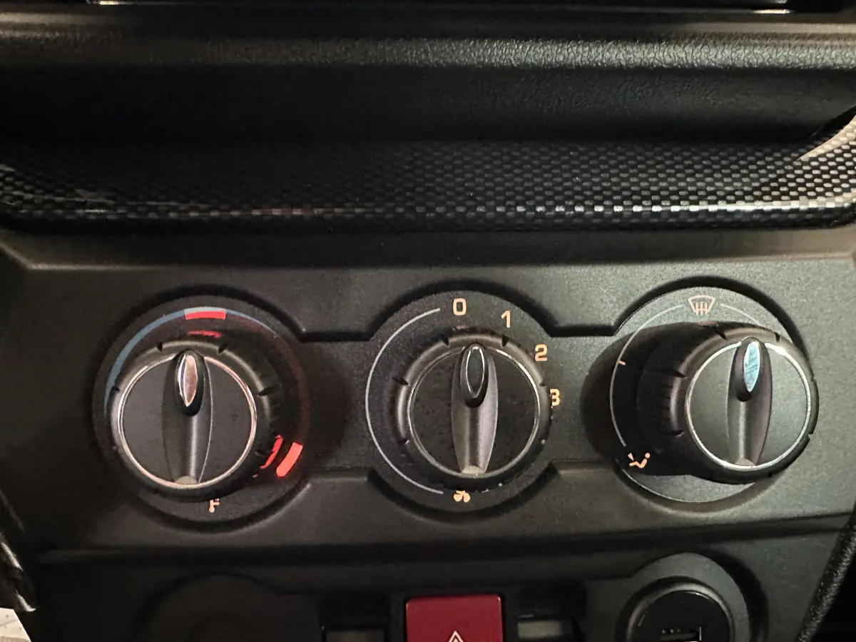 Gros plan sur les commandes de climatisation noires de l'AIXAM Ambition rouge, avec réglages de température, ventilation et désembuage.