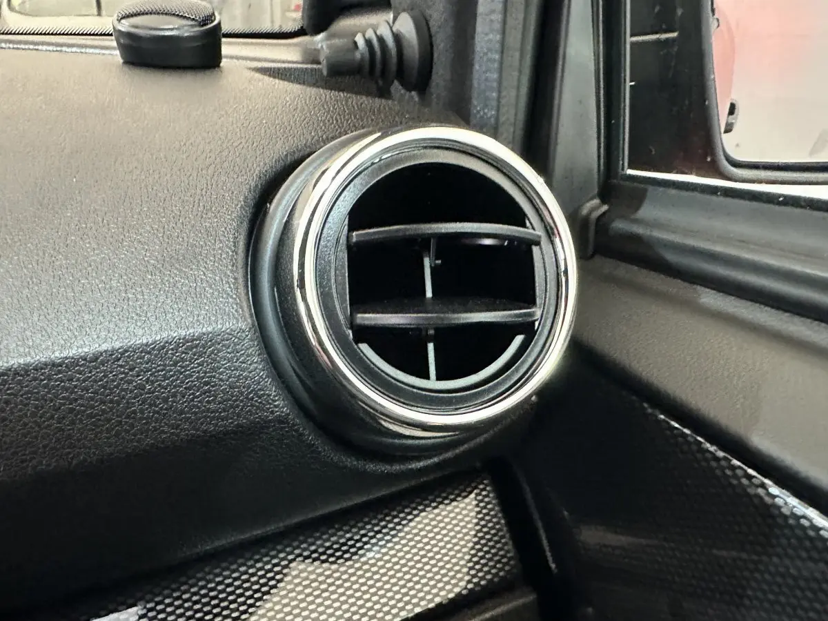 Gros plan sur la sortie d’air ronde chromée côté conducteur de l’AIXAM AMBITION rouge, avec rétroviseur extérieur visible.