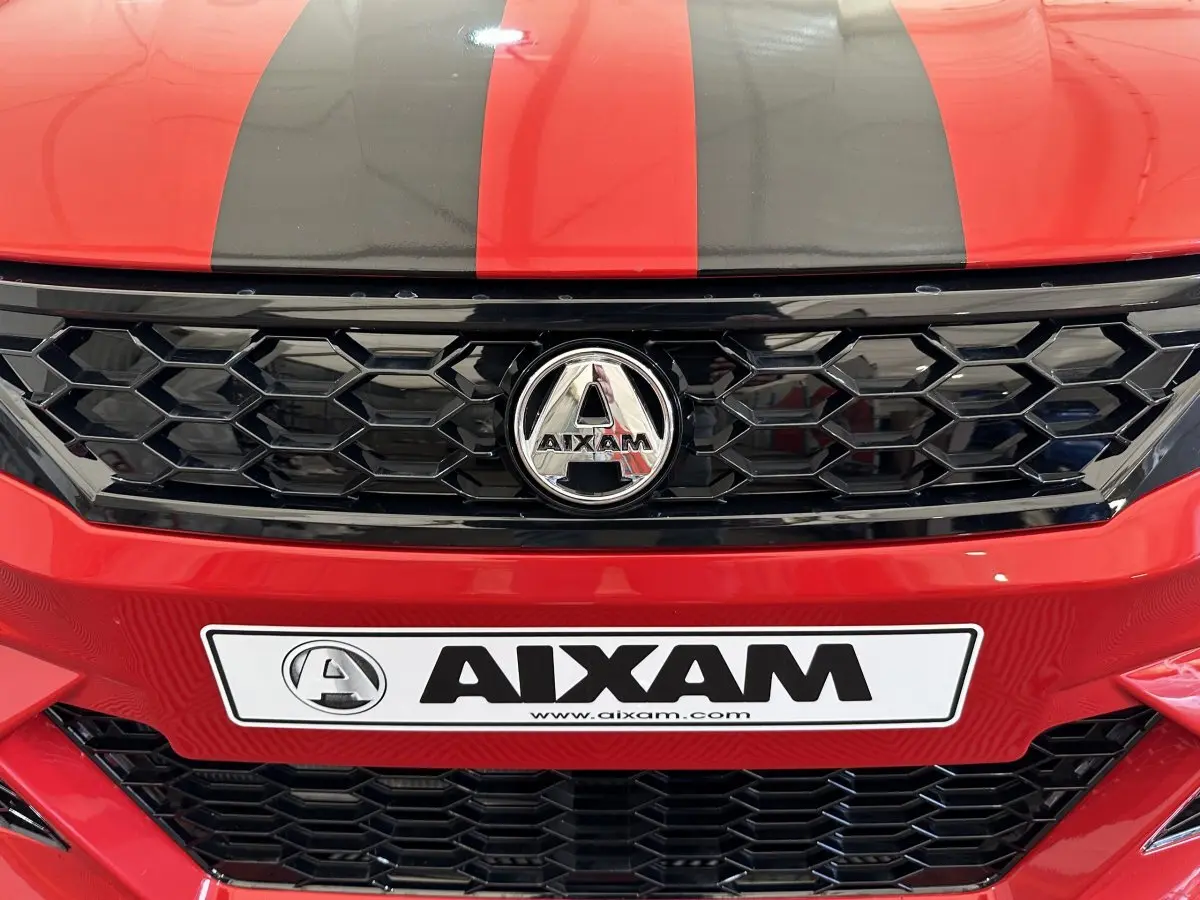Gros plan avant sur la calandre noire et le logo AIXAM d'une AMBITION rouge avec bandes noires sur le capot.