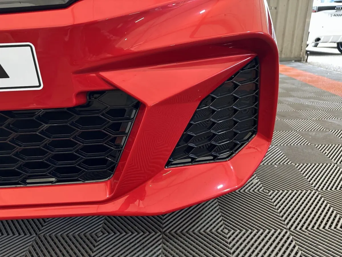 Gros plan sur la calandre avant droite rouge de l'AIXAM AMBITION 0.5 CITY COUPE GTI avec grille noire en nid d'abeille.