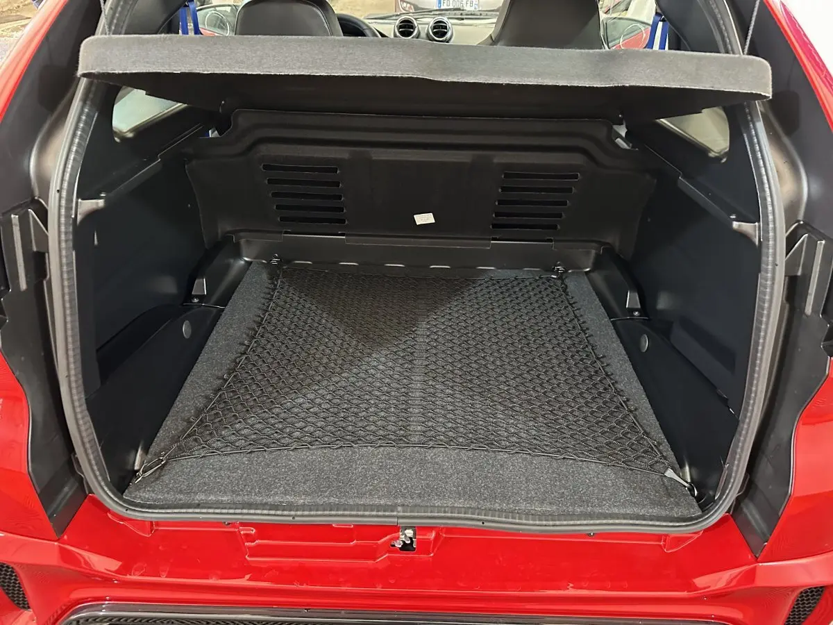 Vue arrière du coffre ouvert d'une Aixam Ambition rouge 2026, avec filet de rangement et intérieur noir.