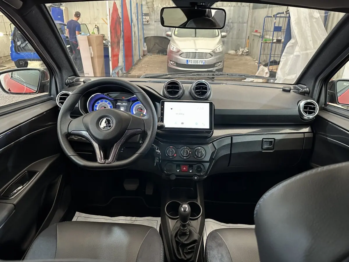 Vue intérieure de face du tableau de bord de l'AIXAM Ambition rouge, avec volant, écran tactile et commandes visibles.