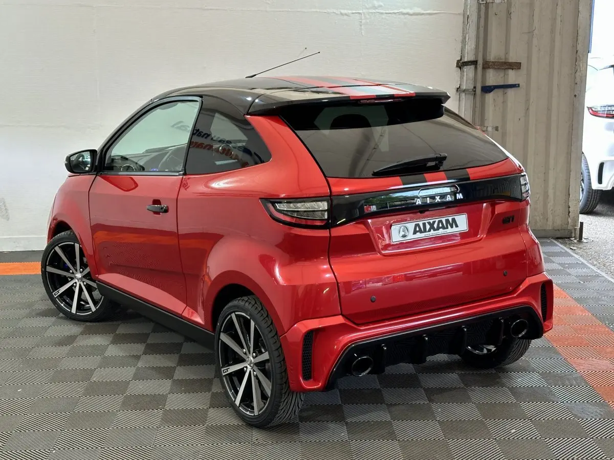 Vue 3/4 arrière droite d'une Aixam Ambition rouge 2026 avec toit noir, jantes noires et bandes rouges sur le toit.
