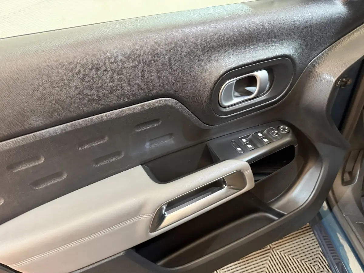 Vue rapprochée de la porte avant gauche d'une Citroën C5 Aircross Hybrid bleu, montrant les commandes électriques et la poignée intérieure.