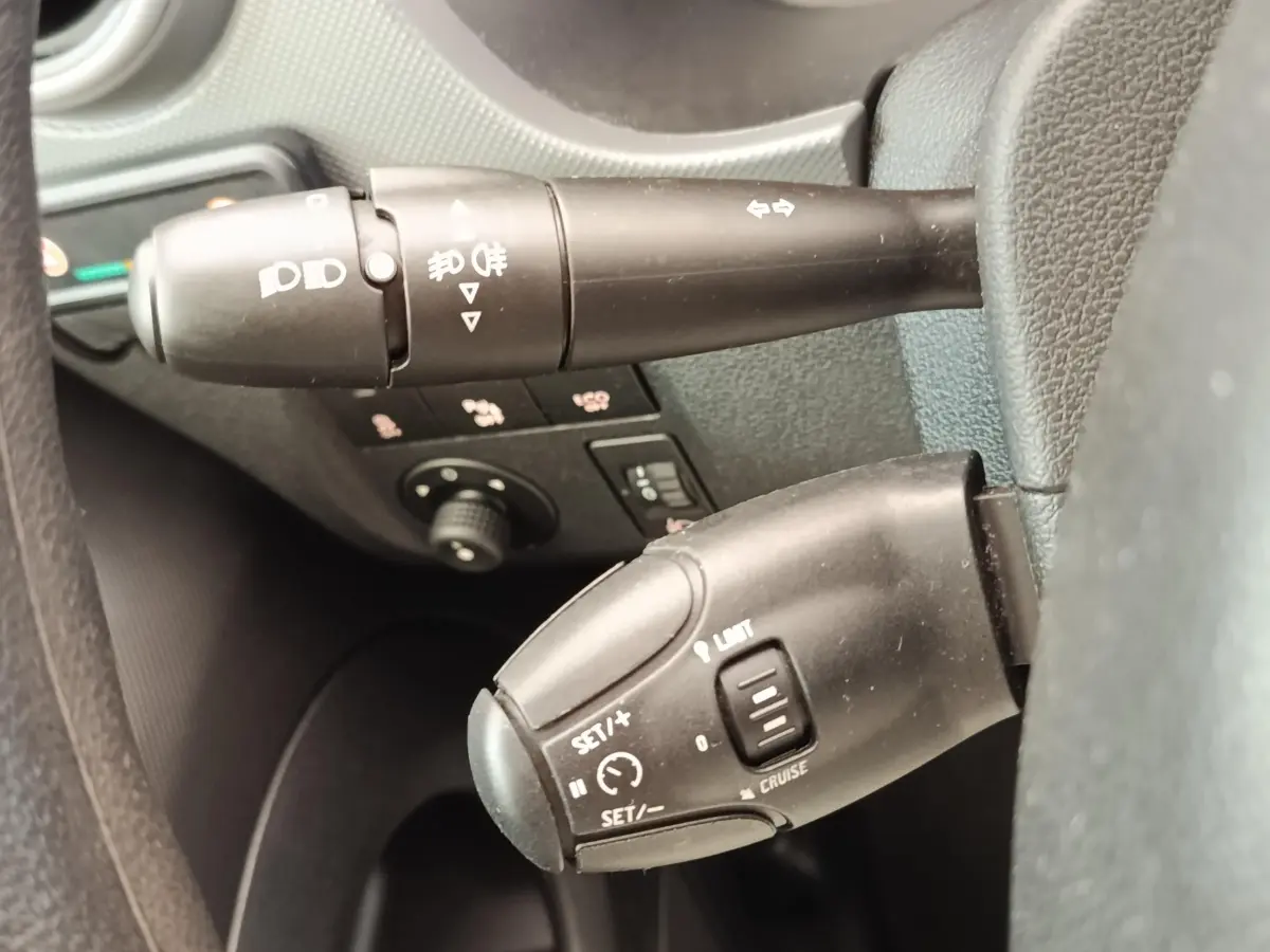 Gros plan sur les commandes au volant du Peugeot Partner blanc, montrant les leviers de clignotants et régulateur de vitesse.