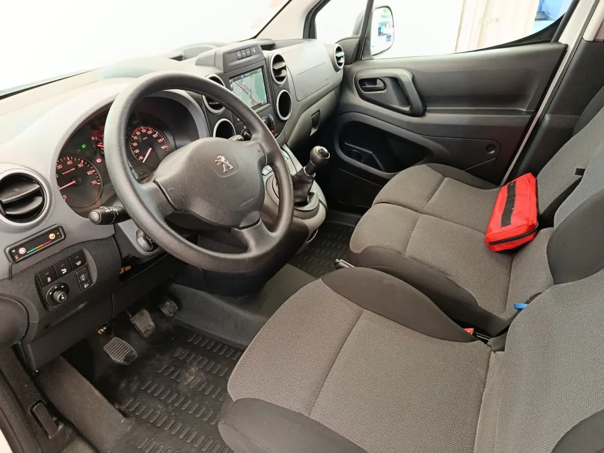 Vue intérieure côté conducteur du Peugeot Partner blanc, montrant le volant, tableau de bord et sièges gris avec trousse rouge.