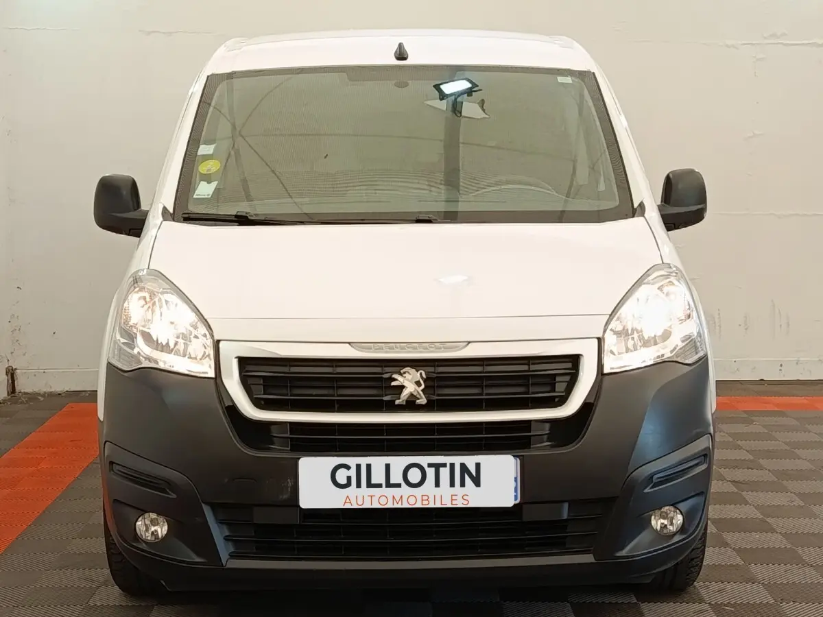 Vue frontale d'un Peugeot Partner blanc 2018 avec pare-chocs noir et phares allumés en intérieur.