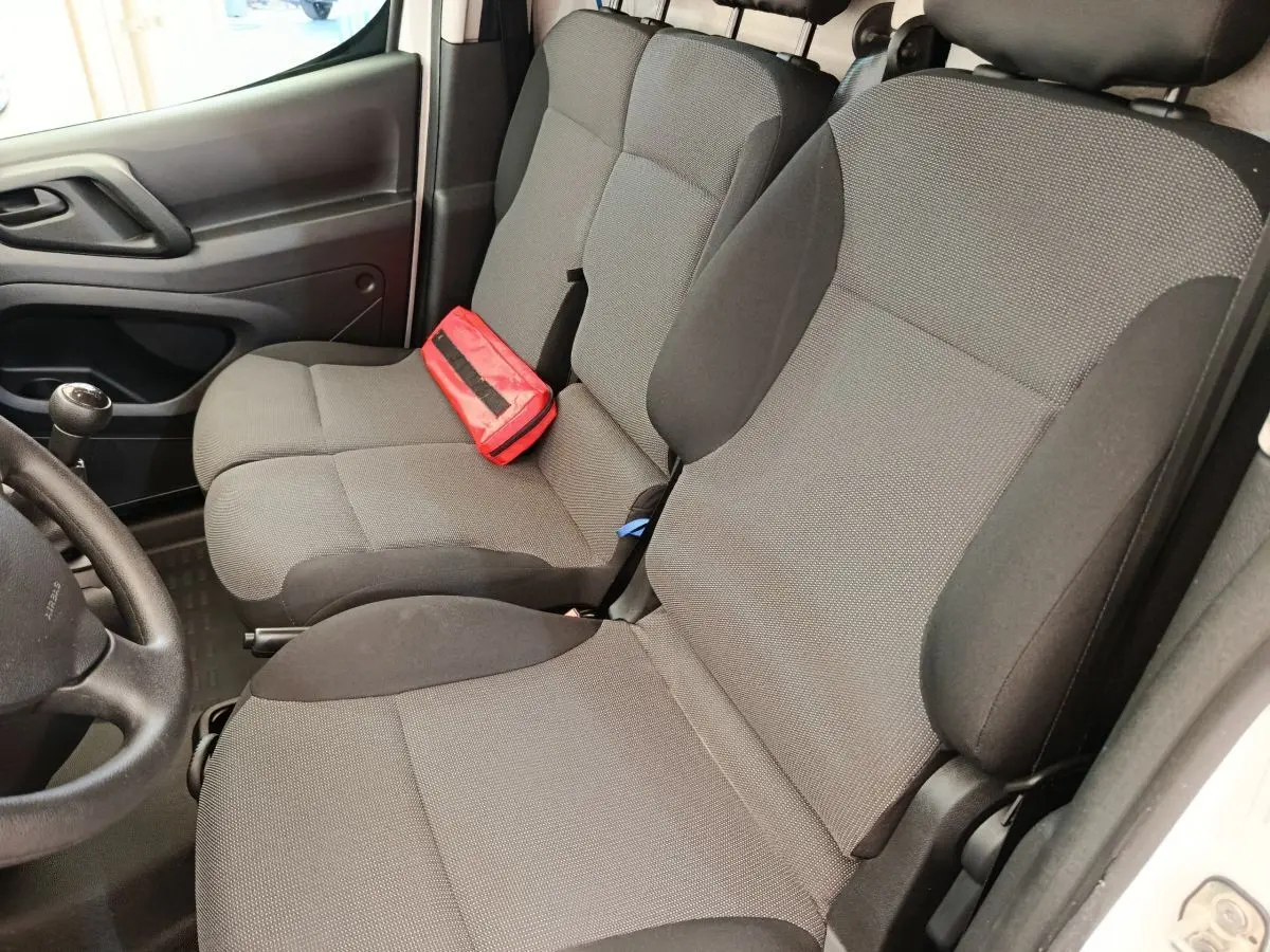 Vue intérieure côté conducteur du Peugeot Partner 1.6 BlueHDi 100, sièges tissu gris avec trousse de secours rouge posée.