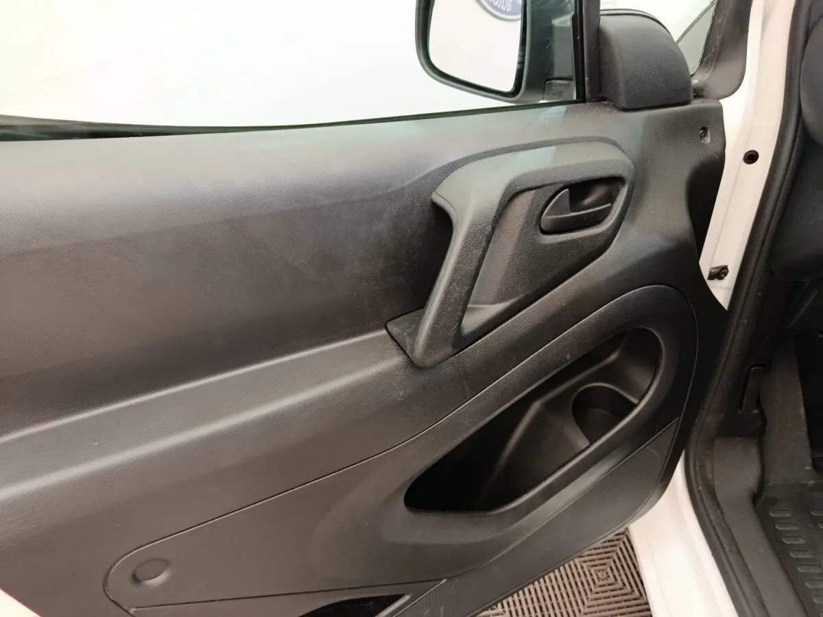 Vue rapprochée de la porte avant gauche noire du Peugeot Partner blanc, avec poignée intégrée et rangement.