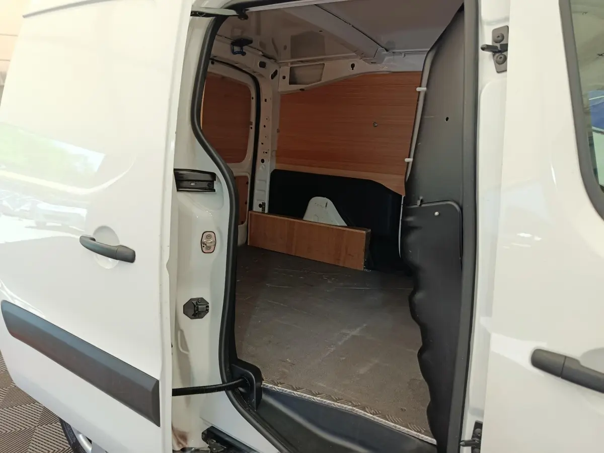 Vue intérieure depuis la porte latérale ouverte du Peugeot Partner blanc, montrant l’espace de chargement avec cloison bois.